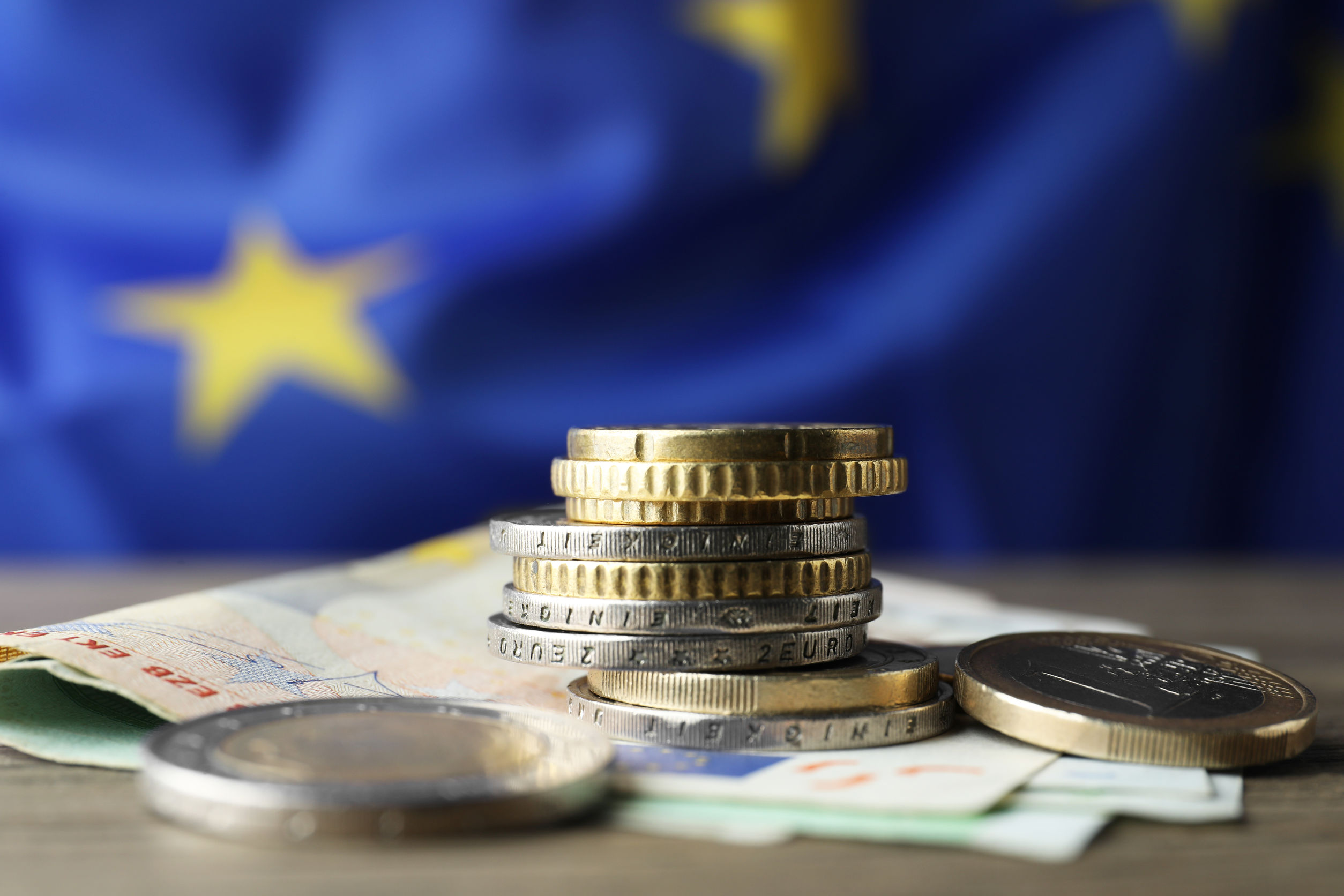 Coins and banknotes on wooden table against European Union flag,